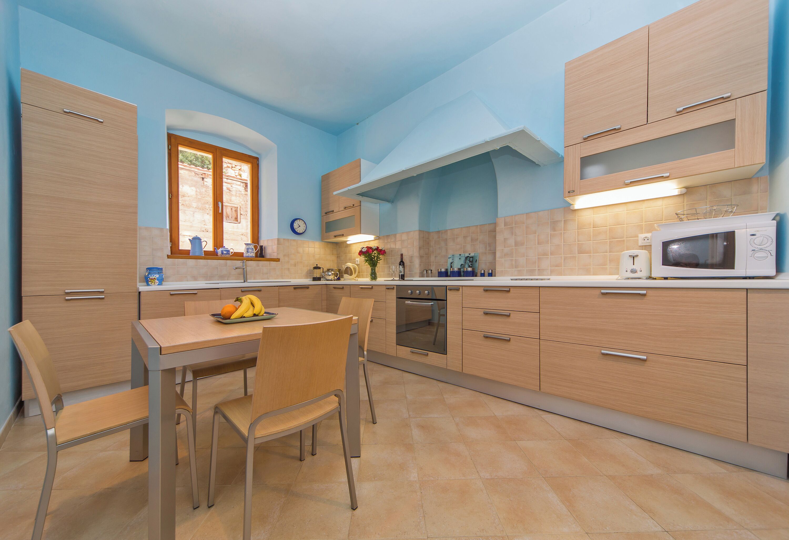 Una cocina moderna con armarios de madera, una mesa de comedor con sillas, un microondas y un ventanal con vistas.