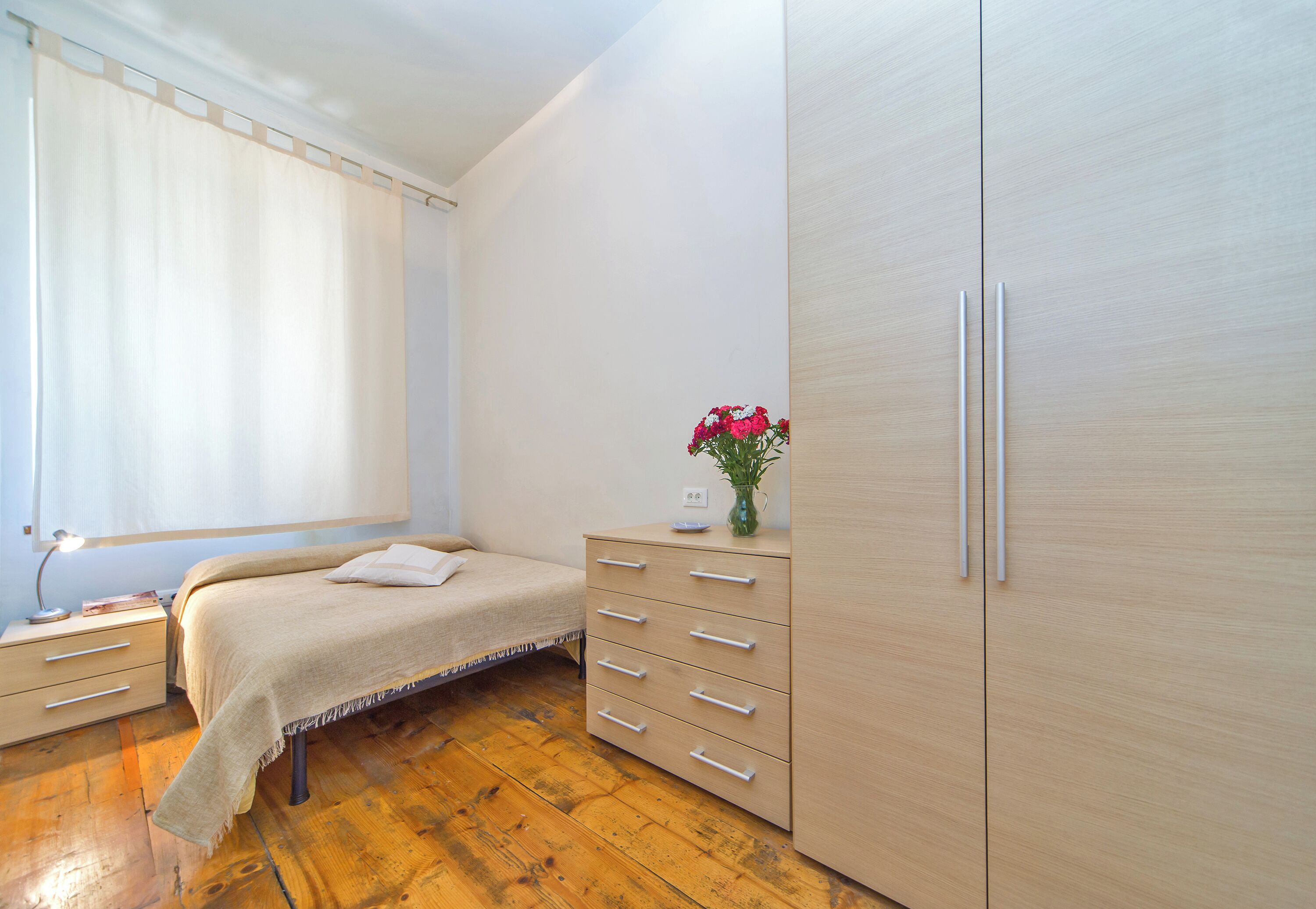 A bedroom with a bed, bedside table, dresser, and a window with curtains.