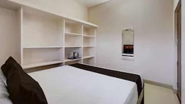 Una camera d'albergo con un letto, un armadio bianco e un piccolo specchio appeso al muro.