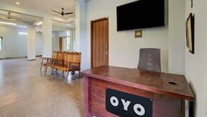 Una reception con un cartello che riporta "OYO" in un'ampia hall con soffitto piatto, una televisione a parete e una porta in legno.