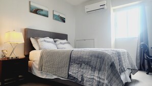 A neatly made bed with a patterned bedspread, a bedside lamp, and two wall-mounted paintings. - Ocean View 1-bedroom apartment with Pool View in heart of Kingston (Kingston)