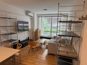 A modern living room with a wooden floor, a sofa, a dining table, and a TV mounted on the wall. - Cozy 1-bedroom apartment in charming Buenos Aires with AC and gym (Buenos Aires)