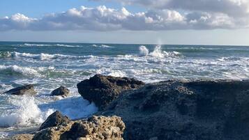 A rocky shoreline with waves crashing against the rocks under a clear sky.