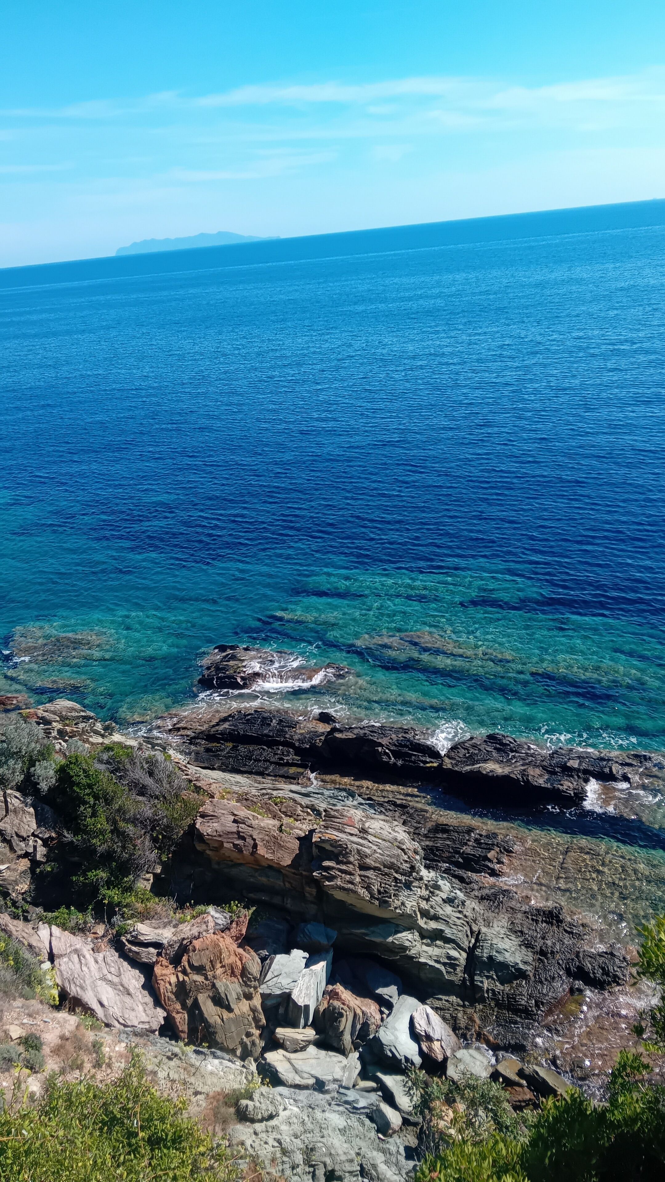 Paesaggio costiero con mare cristallino, scogliere rocciose e vegetazione rada.