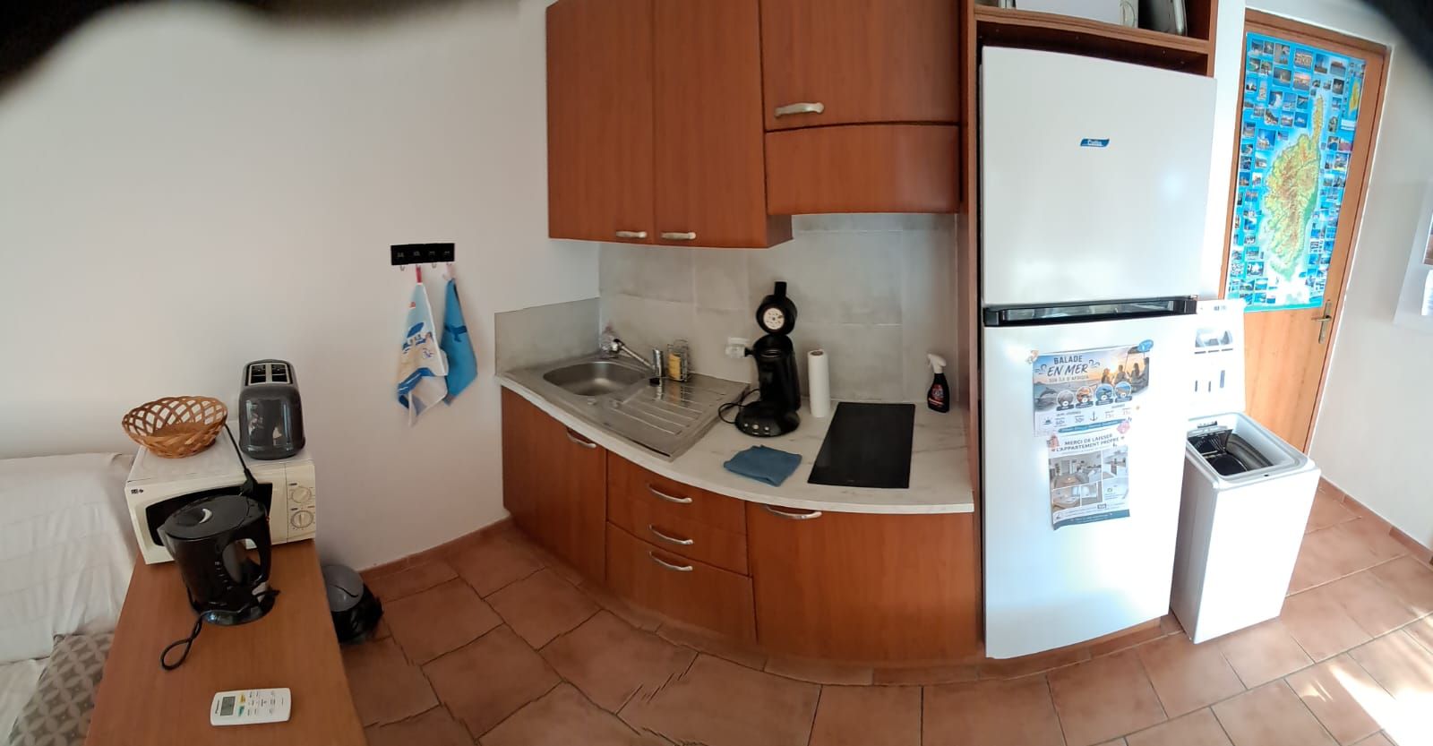 Een kleine keuken met houten kastjes, een witte koelkast, een spoelbak en een betegelde achterwand.
