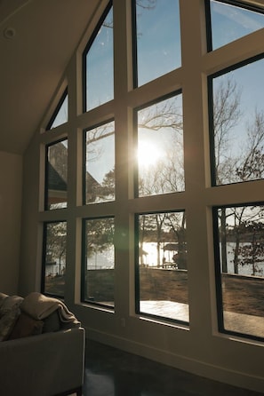 Ein Zimmer mit großen Fenstern, einer Couch und Blick auf einen See und Bäume.