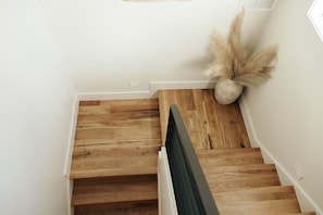 Un escalier en bois avec une rampe noire, des murs blancs et une plante en pot.
