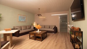 Uma sala de estar moderna com piso de madeira, um sofá seccional, uma mesa de centro e uma TV fixada na parede.