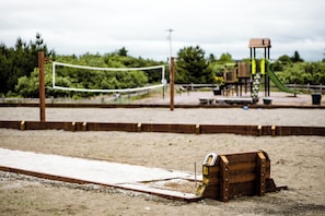 Una playa arenosa con una red de voleibol, juegos de madera y un tobogán.
