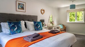 Un lit bien fait, avec une couverture blanche et orange, une tête de lit grise et des coussins décoratifs.