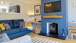 Un salon moderne avec un canapé bleu, une cheminée, un téléviseur fixé au mur et une petite table avec une lampe.