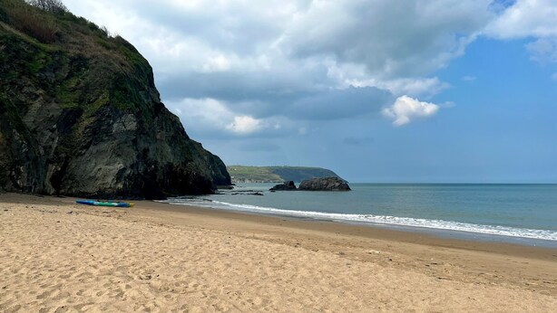 Une plage de sable avec une falaise rocheuse et un kayak.