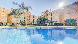 Una piscina con acqua cristallina, circondata da palme e un edificio a più piani con balconi.