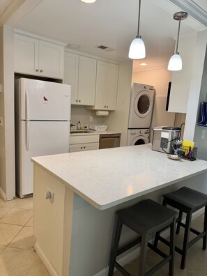 A kitchen with white cabinets, a refrigerator, a washing machine, and a coffee maker.
