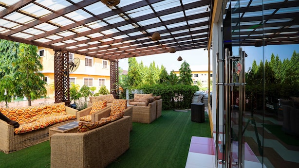 A covered outdoor seating area with wicker furniture and a glass door entrance. - Eastern Plus Hotel  (Somanya)