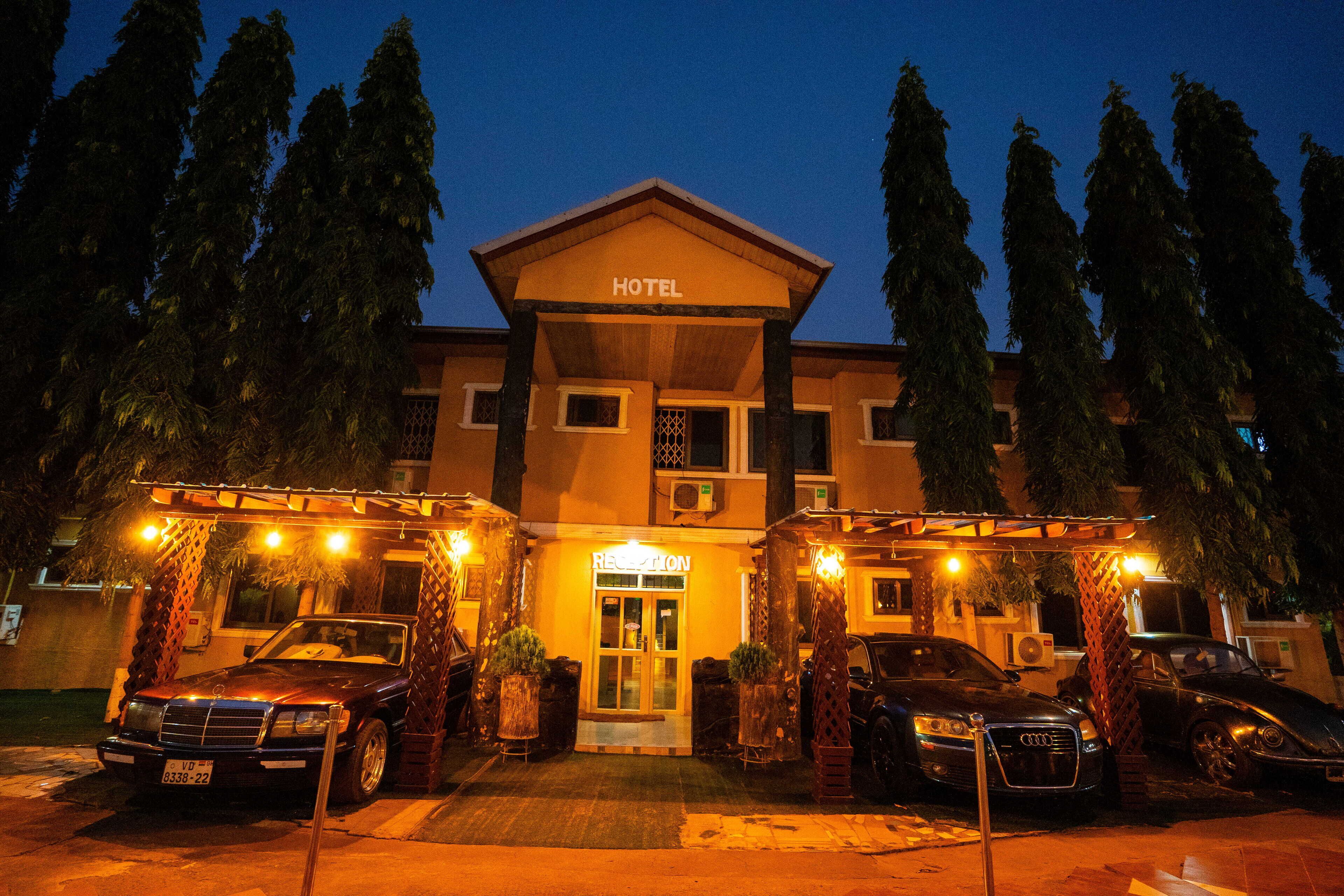A hotel with a reception area, a parking lot with several cars, and a well-lit entrance.