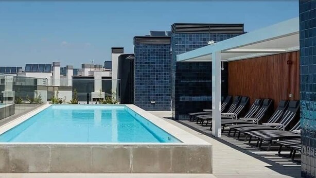 A rooftop pool with a city view, lounge chairs, and a glass barrier. - Baia Rio by Proud Progress Homes (Seixal)