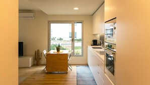 A modern kitchen with a dining area, large windows, and a view of the outdoors. - Baia Rio by Proud Progress Homes (Seixal)