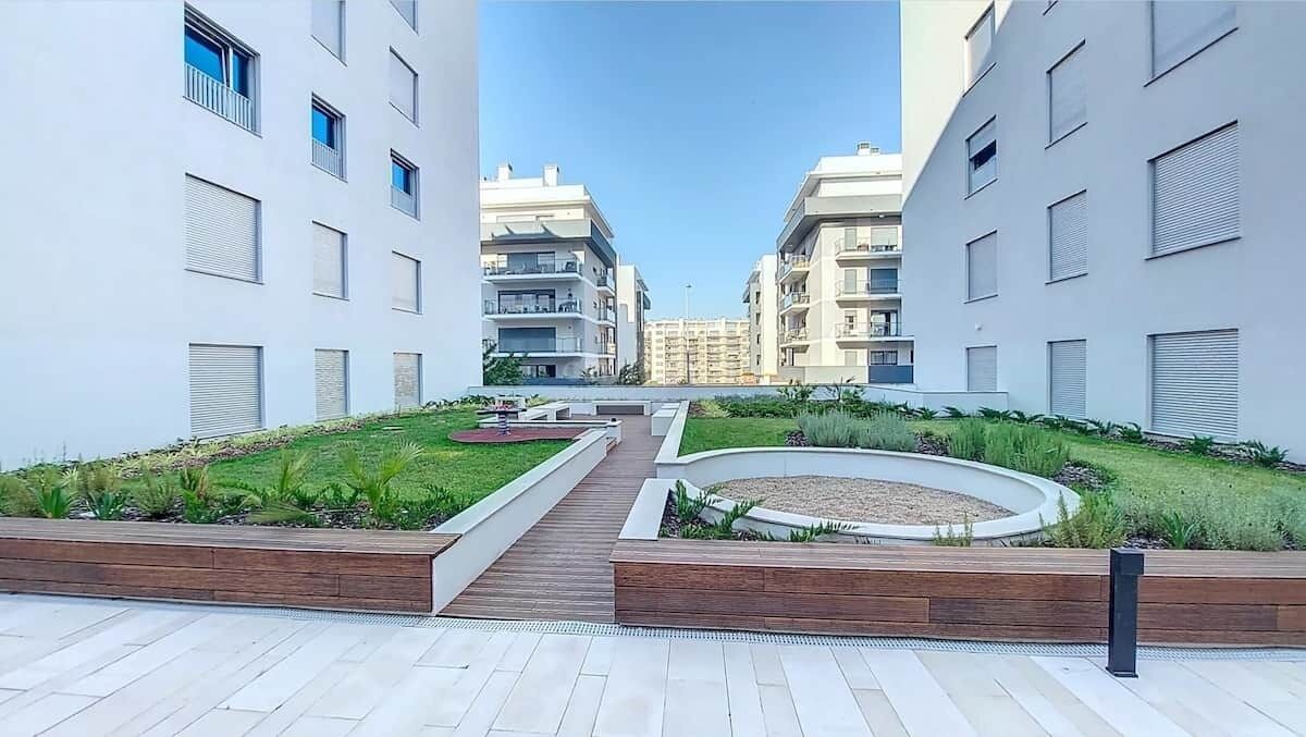 A modern residential complex with a central landscaped area, featuring a circular garden and a wooden pathway.
