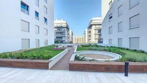A modern residential complex with a central landscaped area, featuring a circular garden and a wooden pathway. - Baia Rio by Proud Progress Homes (Seixal)