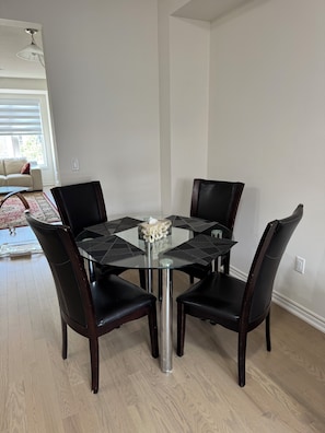 Un comedor con una mesa de vidrio rodeada por cuatro sillas de cuero oscuro.