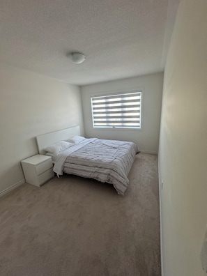 Un dormitorio con cama, mesita de noche, ventana con persianas y lámpara en el techo.