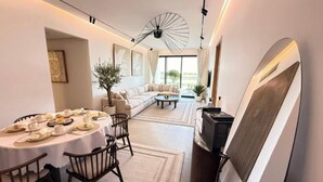 A modern hotel room with a dining area, a sofa, and a large window.