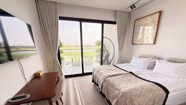 A hotel room with a bed, a desk, a chair, a TV, and a large window with a view of a green landscape.