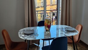 En spiseplads med et rundt bord, to stole, en vase med blomster og udsigt til bygninger gennem store vinduer.