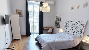 Et soveværelse med seng, skrivebord, stol, hængende lampe og et vindue med gardiner.