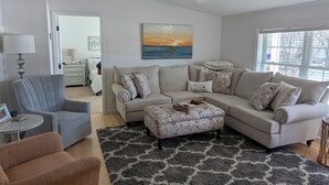 A living room with a beige sectional sofa, a grey armchair, a patterned ottoman, and a black and white rug. - Incredible 3-bedroom house WITH BOAT DOCK on Rehoboth Bay (Millsboro)