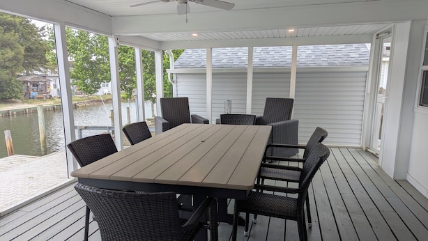 A covered outdoor deck with a table and chairs, a ceiling fan, and a view of a body of water. - Incredible 3-bedroom house WITH BOAT DOCK on Rehoboth Bay (Millsboro)