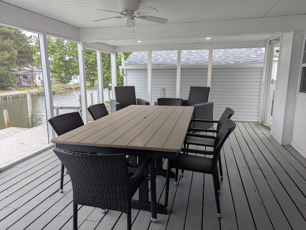 A covered outdoor deck with a table and chairs, a ceiling fan, and a view of a body of water. - Incredible 3-bedroom house WITH BOAT DOCK on Rehoboth Bay (Millsboro)