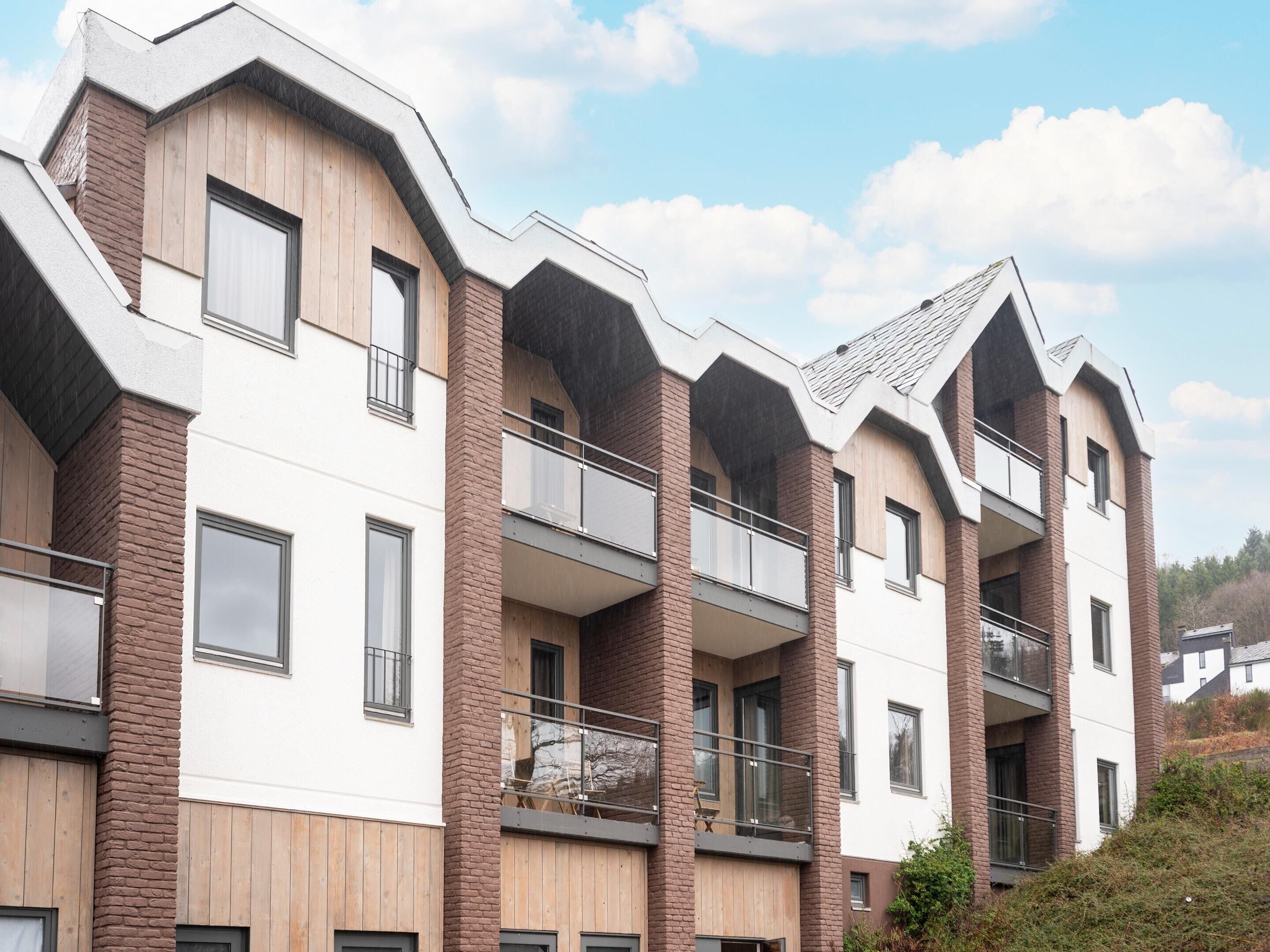 A modern multi-story residential building with balconies, large windows, and a brick facade.