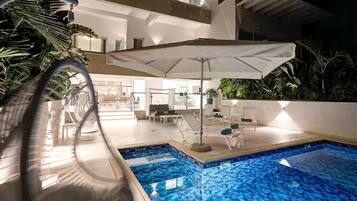 Una piscina interior con vistas despejadas al área de descanso contigua, un parasol grande y un diseño arquitectónico moderno.