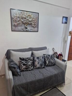 A grey sofa with patterned cushions, a framed floral artwork above it, and a small table with a telephone and bags. - The best loft in Lapa, comfort and tranquility in the middle of Rio's best Carnival. (Rio de Janeiro)