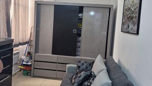 Een woonkamer met een grijze bank, een plafondventilator en een garderobe met spiegel.