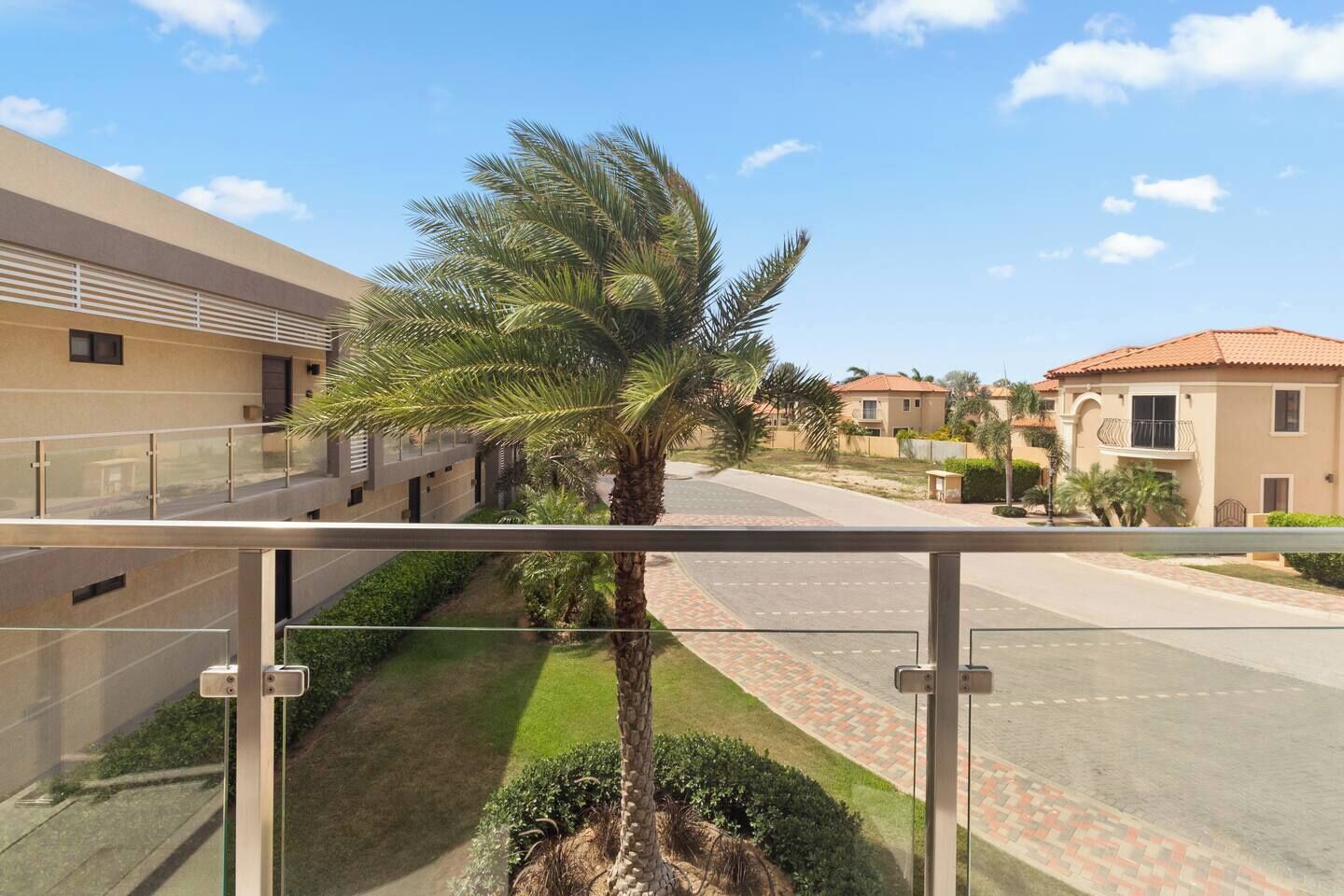 Un barrio residencial con cielo despejado, una palmera y casas con techos de tejas rojas.