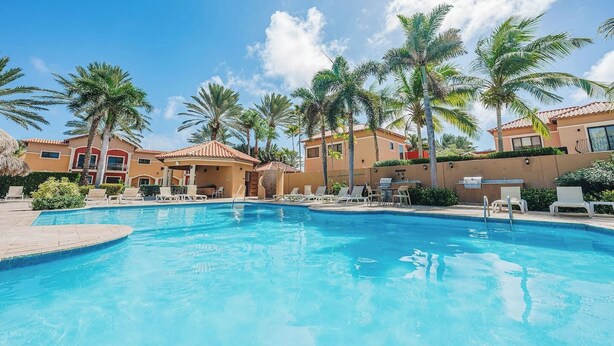 A pool area with lounge chairs and palm trees, surrounded by buildings with a Mediterranean architectural style. - Stylish Gold Coast Condo Sunrise by Bocobay (Noord)