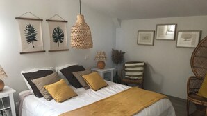 Un dormitori amb un llit gran, molcalins, una làmpada penjant, una cadira i obra d'art emmarcada a la paret.