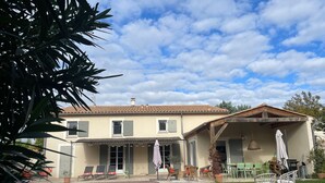 Una casa de dues plantes amb piscina, zona de seients a l'exterior i un porxo cobert.