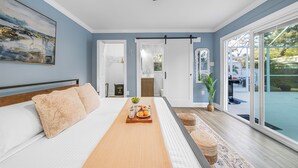Ein Schlafzimmer mit Bett, Frühstückswagen, großem Fenster und Blick ins Freie.