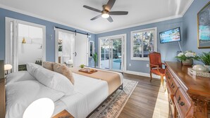 Ein Schlafzimmer mit Bett, Deckenventilator, Fernseher, Stuhl und Kommode.