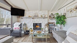Ein gemütliches Wohnzimmer mit Kamin aus Stein, bequemen Sitzmöglichkeiten, einem Flachbildfernseher und einem Bücherregal.