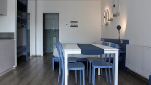 Une pièce moderne et bien éclairée, comprenant une table à manger, des chaises et un lit. On y trouve également un porte-manteau et un luminaire fixé au mur.