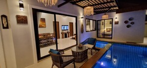 A modern indoor swimming pool area with a glass table and wicker chairs, a ceiling with exposed beams, and a large window with a view of the pool. - Luxury Private Pool Villa for 10 Guests – 8 Mins to Ao Nang Beach" (Ao Nang)