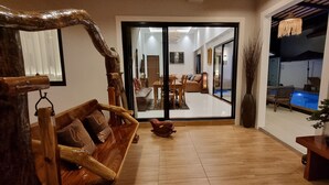 Ein großzügiger Wohnbereich mit einer Holzbank, einem kleinen Tisch und einem Blumentopf. Eine Glastür führt zu einem Balkon mit einem Pool.