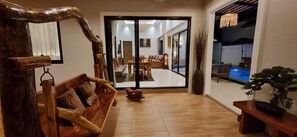 A spacious living area with a wooden bench, a small table, and a potted plant. A sliding glass door leads to a balcony with a pool. - Luxury Private Pool Villa for 10 Guests – 8 Mins to Ao Nang Beach" (Ao Nang)