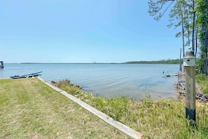A calm lake with boats, a grassy area, and a wooden post with a birdhouse. - Cozy Bayfront Guest Cottage - Boat Friendly Dock! (Elberta)