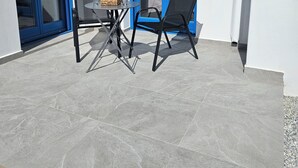 En terrasse med et bord og to stole, en glasdør og en blå ramme.